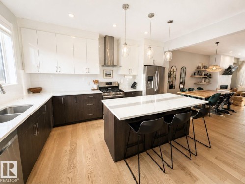 Wood-finish flooring, two-tone cabinetry with bright white upper cabinets and dark lower cabinets, white countertops, stainless steel appliances, and a central island with integrated seating - 10516 76 Street Nw, Edmonton, AB 