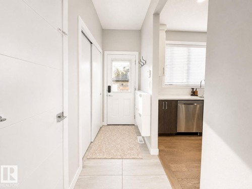 Entryway with light tile flooring, leading to a kitchen with wood-finish flooring - 10516 76 Street Nw, Edmonton, AB 
