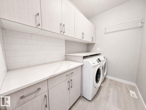 Full-size washer and dryer, tile flooring, solid surface countertops, extensive upper and lower cabinetry, and subway tile backsplash - 10516 76 Street Nw, Edmonton, AB 
