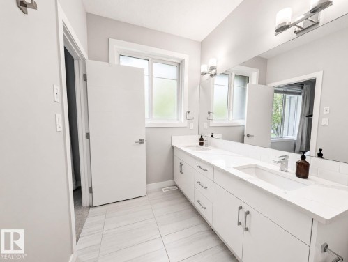 Dual vanity with integrated sinks and white countertops, under-vanity storage, large wall-mounted mirror, and tile flooring - 10516 76 Street Nw, Edmonton, AB 