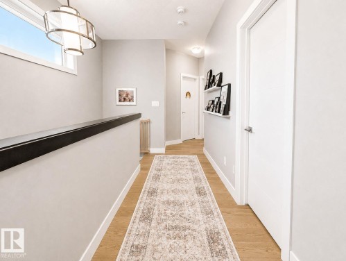 Wood-finish flooring, contemporary light fixture, modern white doors, minimalist wall shelving, and a horizontal transom window - 10516 76 Street Nw, Edmonton, AB 