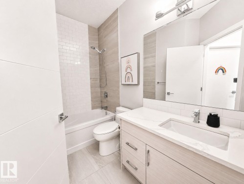 Bathroom featuring a built-in bathtub, subway tile wall, large vanity mirror, single basin sink, and tile flooring - 10516 76 Street Nw, Edmonton, AB 