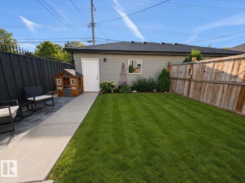 Expansive lawn area with a concrete pathway, privacy fencing, and a detached structure featuring siding and a white entry door - 10516 76 Street Nw, Edmonton, AB 
