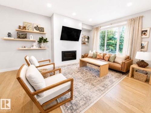Recessed lighting illuminates the open living area featuring wood-finish flooring, a built-in fireplace, and expansive windows - 10516 76 Street Nw, Edmonton, AB 