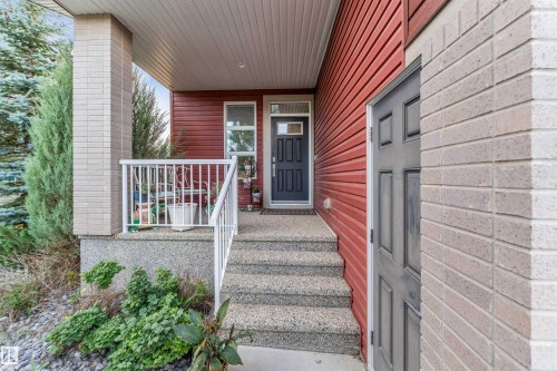 Red horizontal siding exterior with a dark gray paneled entry door - 718 Charlesworth Way Sw, Edmonton, AB 