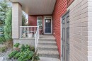 Red horizontal siding exterior with a dark gray paneled entry door - 718 Charlesworth Way Sw, Edmonton, AB 