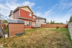 Red siding exterior with white trim, a rear wooden deck, a detached shed with shingle roofing, and a wooden perimeter fence - 