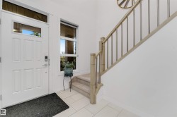 White paneled entry door with transom and sidelight, tile flooring, and carpeted stairs with a wood and metal railing - 
