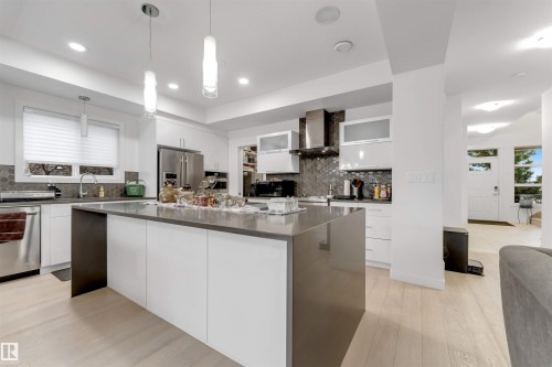 Gourmet kitchen featuring a large central island, white cabinetry, stainless steel appliances, and a unique backsplash - 718 Charlesworth Way Sw, Edmonton, AB 