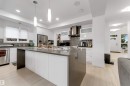 Gourmet kitchen featuring a large central island, white cabinetry, stainless steel appliances, and a unique backsplash - 718 Charlesworth Way Sw, Edmonton, AB 
