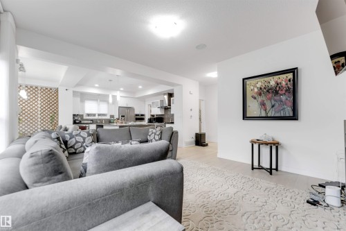 Open-concept living area featuring light wood-finish flooring, recessed lighting, and a kitchen with stainless steel appliances - 718 Charlesworth Way Sw, Edmonton, AB 