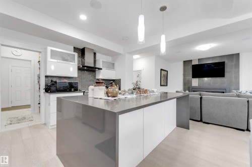 Kitchen featuring a large island with a stone-finish countertop, white cabinetry, and stainless steel appliances - 718 Charlesworth Way Sw, Edmonton, AB 