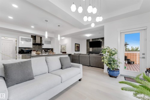 Open-concept living area featuring light wood-finish flooring, recessed lighting, and a modern chandelier - 718 Charlesworth Way Sw, Edmonton, AB 