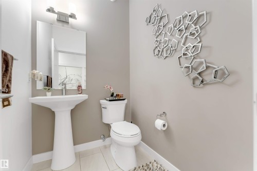 Pedestal sink, wall-mounted mirror, brushed nickel light fixture, tile flooring, and a contemporary wall art installation - 718 Charlesworth Way Sw, Edmonton, AB 