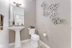 Pedestal sink, wall-mounted mirror, brushed nickel light fixture, tile flooring, and a contemporary wall art installation - 