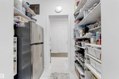 Walk-in pantry with extensive shelving, white tile flooring, and a stainless steel refrigerator - 718 Charlesworth Way Sw, Edmonton, AB 