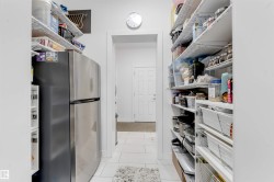Walk-in pantry with extensive shelving, white tile flooring, and a stainless steel refrigerator - 