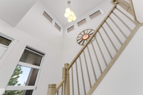 Soaring two-story ceiling with multiple clerestory windows, a contemporary multi-bulb pendant light, and a staircase featuring a wood-finish handrail with metal balusters - 718 Charlesworth Way Sw, Edmonton, AB 