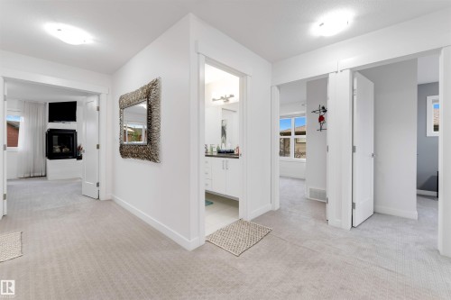 Recessed fireplace with hearth, white built-in cabinetry, light-toned carpeting, and multiple doorways - 718 Charlesworth Way Sw, Edmonton, AB 