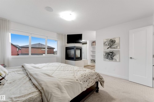 Expansive window with white trim, built-in fireplace, recessed ceiling speaker, white interior door with modern hardware, and light-colored carpet flooring - 718 Charlesworth Way Sw, Edmonton, AB 
