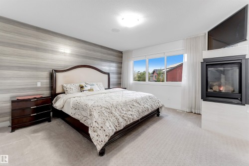 Integrated fireplace with a white tile surround, large windows, light-colored carpeting, and a distinctive accent wall - 718 Charlesworth Way Sw, Edmonton, AB 