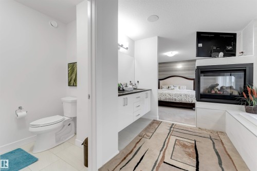 Built-in fireplace with a hearth, white vanity with dual sinks, and an integrated toilet - 718 Charlesworth Way Sw, Edmonton, AB 
