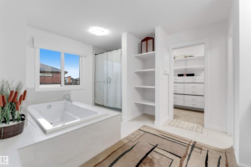 Built-in soaking tub with deck, glass-enclosed shower, built-in shelving, and entry to a separate walk-in closet with built-in drawers and shelving - 718 Charlesworth Way Sw, Edmonton, AB 