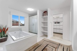 Built-in soaking tub with deck, glass-enclosed shower, built-in shelving, and entry to a separate walk-in closet with built-in drawers and shelving - 