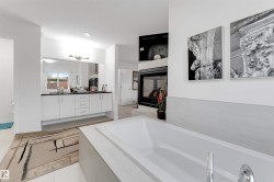 White soaking tub with deck-mounted chrome faucet, light-toned wall tile, and a built-in fireplace - 