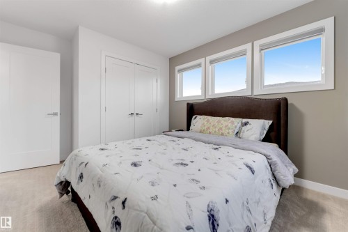 Bedroom featuring three horizontal windows, neutral wall tones, white trim, and light-toned carpeting - 718 Charlesworth Way Sw, Edmonton, AB 