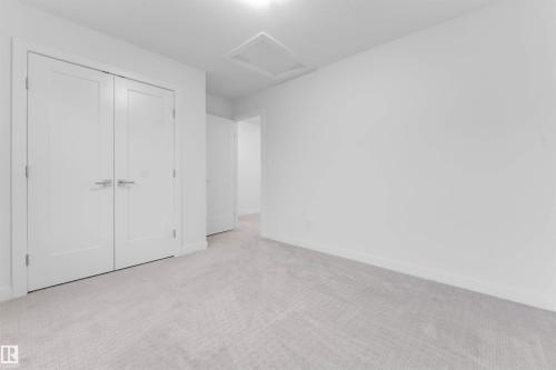 White interior with light grey patterned carpet, featuring a flush mount ceiling light and white double doors with brushed nickel hardware - 718 Charlesworth Way Sw, Edmonton, AB 