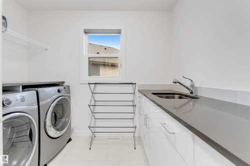 White cabinetry with stainless steel hardware, dark countertop, and an undermount sink with a chrome faucet - 718 Charlesworth Way Sw, Edmonton, AB 