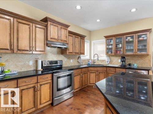 Kitchen featuring wood-finish cabinetry, black countertops, tile backsplash, and stainless steel appliances - 496 Ravine Court, Devon, AB 