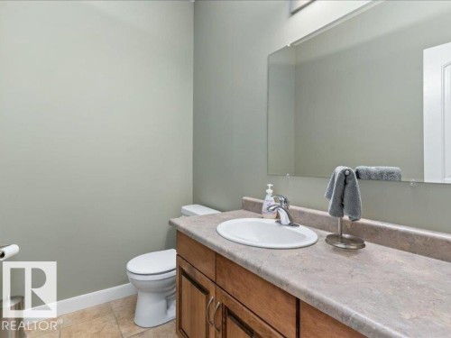 Built-in vanity with wood-finish cabinetry, integrated sink, and an expansive mirror - 496 Ravine Court, Devon, AB 