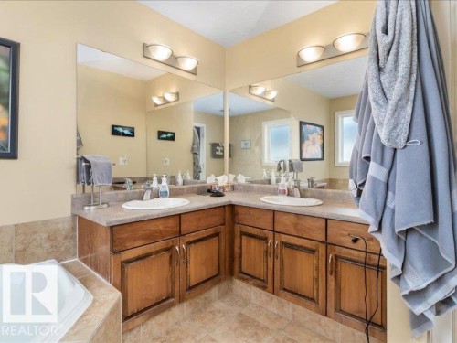 Dual vanity with wood-finish cabinetry, integrated sinks, and individual light fixtures - 496 Ravine Court, Devon, AB 