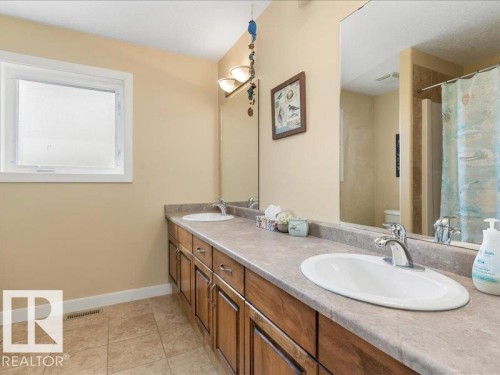 Dual vanity with wood-finish cabinetry and integrated sinks, complemented by a large wall-mounted mirror - 496 Ravine Court, Devon, AB 