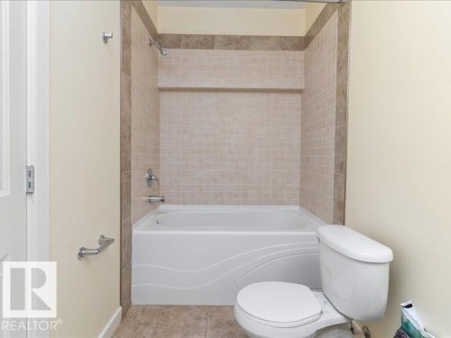 Tiled shower surround with decorative accent band, integrated showerhead, and bathtub with contemporary detailing - 496 Ravine Court, Devon, AB 
