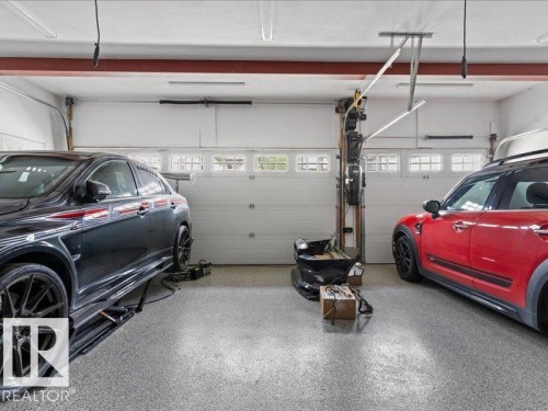 Spacious garage with two overhead doors featuring transom windows, fluorescent lighting, and a durable epoxy-coated floor - 496 Ravine Court, Devon, AB 