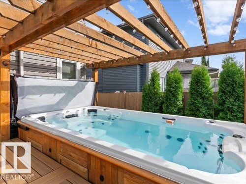 Wood pergola with integrated lighting, built-in swim spa, wood deck, and privacy landscaping - 496 Ravine Court, Devon, AB 