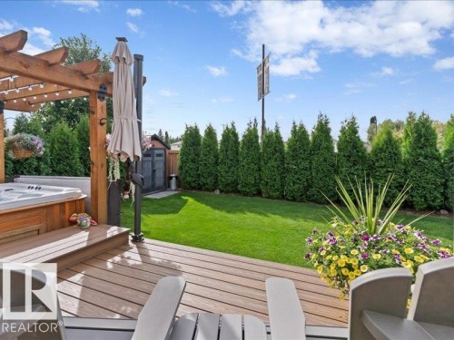Expansive backyard featuring a composite deck, an integrated hot tub, a wood pergola, a manicured lawn, and a storage shed - 496 Ravine Court, Devon, AB 