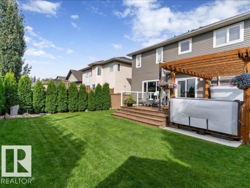 Expansive green lawn with mature evergreen trees, leading to a multi-level wooden deck - 496 Ravine Court, Devon, AB 