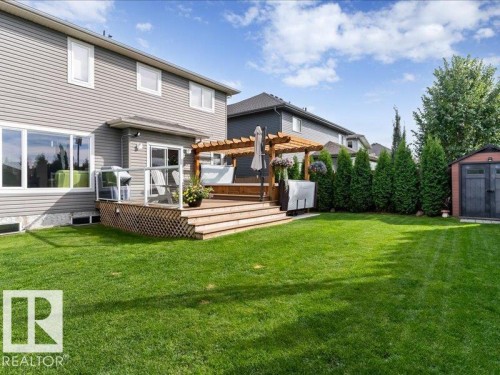 Expansive backyard featuring a large wooden deck with a pergola, mature privacy trees, and a storage shed - 496 Ravine Court, Devon, AB 
