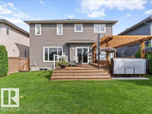 Expansive green lawn with a multi-level wood deck, glass railing, and a wood pergola - 496 Ravine Court, Devon, AB 