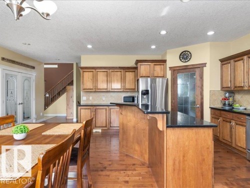 Kitchen featuring wood-finish cabinetry, black countertops, stainless steel appliances, and a tiled backsplash - 496 Ravine Court, Devon, AB 