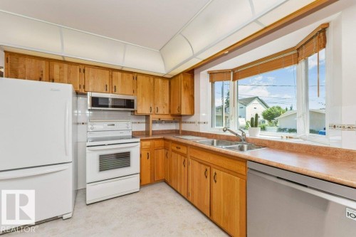 Kitchen featuring wood cabinetry, white appliances, dual basin sink, and a bay window - 11415 56 Avenue Nw, Edmonton, AB 