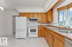 Functional kitchen featuring wood cabinetry, white appliances, dual basin sink, and ample natural light from a large window - 