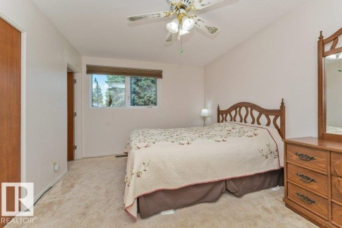 Carpeted bedroom with a built-in ceiling fan, window with exterior foliage, and a wood-finish door - 11415 56 Avenue Nw, Edmonton, AB 