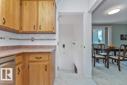 Kitchen featuring wood cabinetry, white tile backsplash with decorative accent, and a built-in stainless steel dishwasher - 11415 56 Avenue Nw, Edmonton, AB 