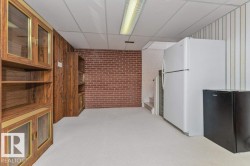 Lower-level room featuring wood-finish cabinetry with glass inserts, exposed brick accent wall, drop ceiling, and carpet flooring - 