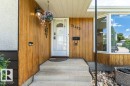 Front entry featuring a white paneled door with glass insert, concrete steps, wood-finish paneling, and a prominent bay window - 11415 56 Avenue Nw, Edmonton, AB 